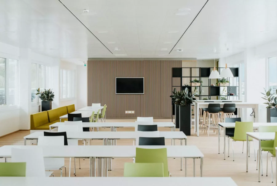 Modernes Betriebsrestaurant mit weißen Tischen, bunten Stühlen, Pflanzen und Fernseher an Holzlamellenwand in Salzburg