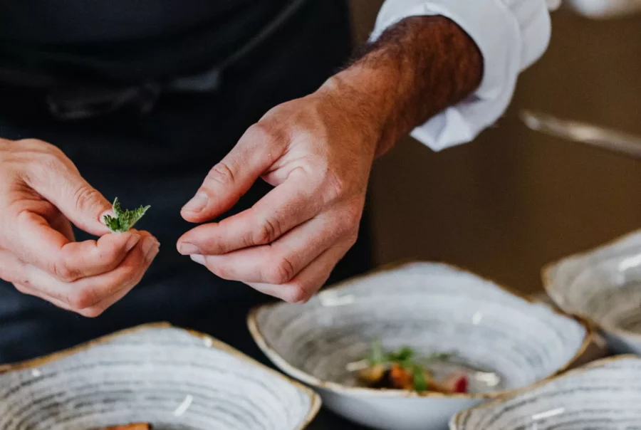 Koch dekoriert mit Kräutern mehrere Schalen mit feinem Essen im Betriebsrestaurant Cateringservice in Salzburg und