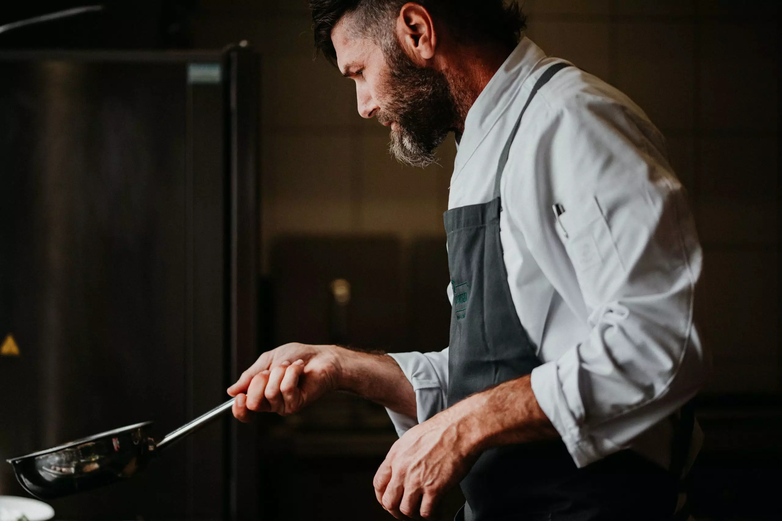 Koch im Betriebsrestaurant konzentriert sich beim Zubereiten von Speisen mit Pfanne in professioneller Küche in Salzburg