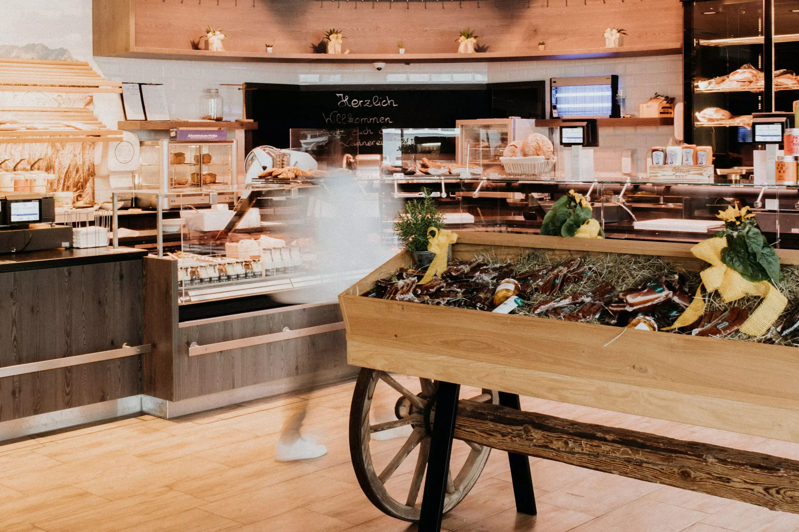 Innenansicht eines Betriebsrestaurants mit Holztheken, Brotregalen und einem Wagen mit verpackten Lebensmitteln in Salzburg.