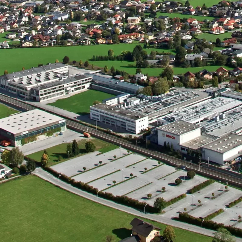 Luftaufnahme eines Industriegebiets mit Bosch-Werk, umgeben von Wohnhäusern und grünen Wiesen in Salzburg oder