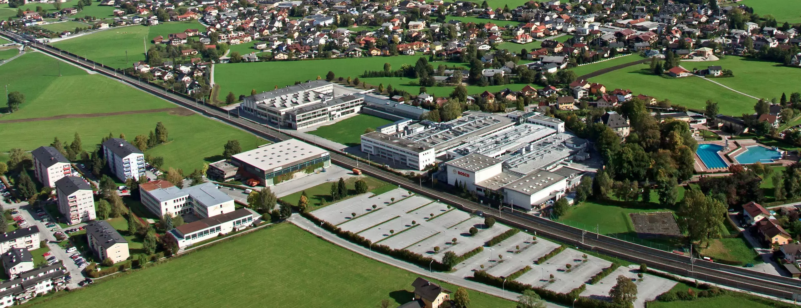 Luftaufnahme eines Industriegebiets mit Bosch-Werk, umgeben von Wohnhäusern und grünen Wiesen in Salzburg oder