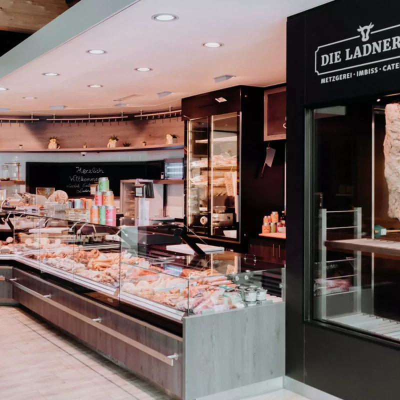 Innenansicht der Ladnerei Metzgerei mit Theke voller Fleisch- und Wurstwaren, Cateringservice und Betriebsrestaurant